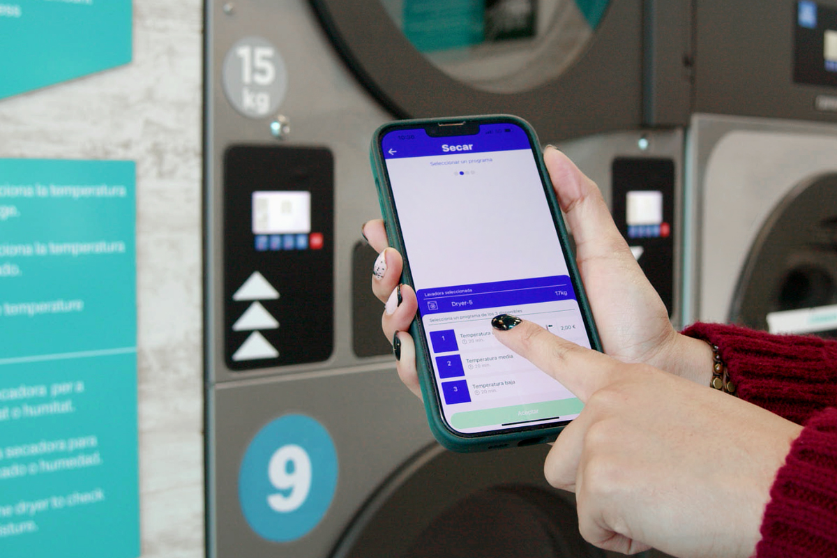 Mano che preme l’app mobile per attivare la lavatrice self-service